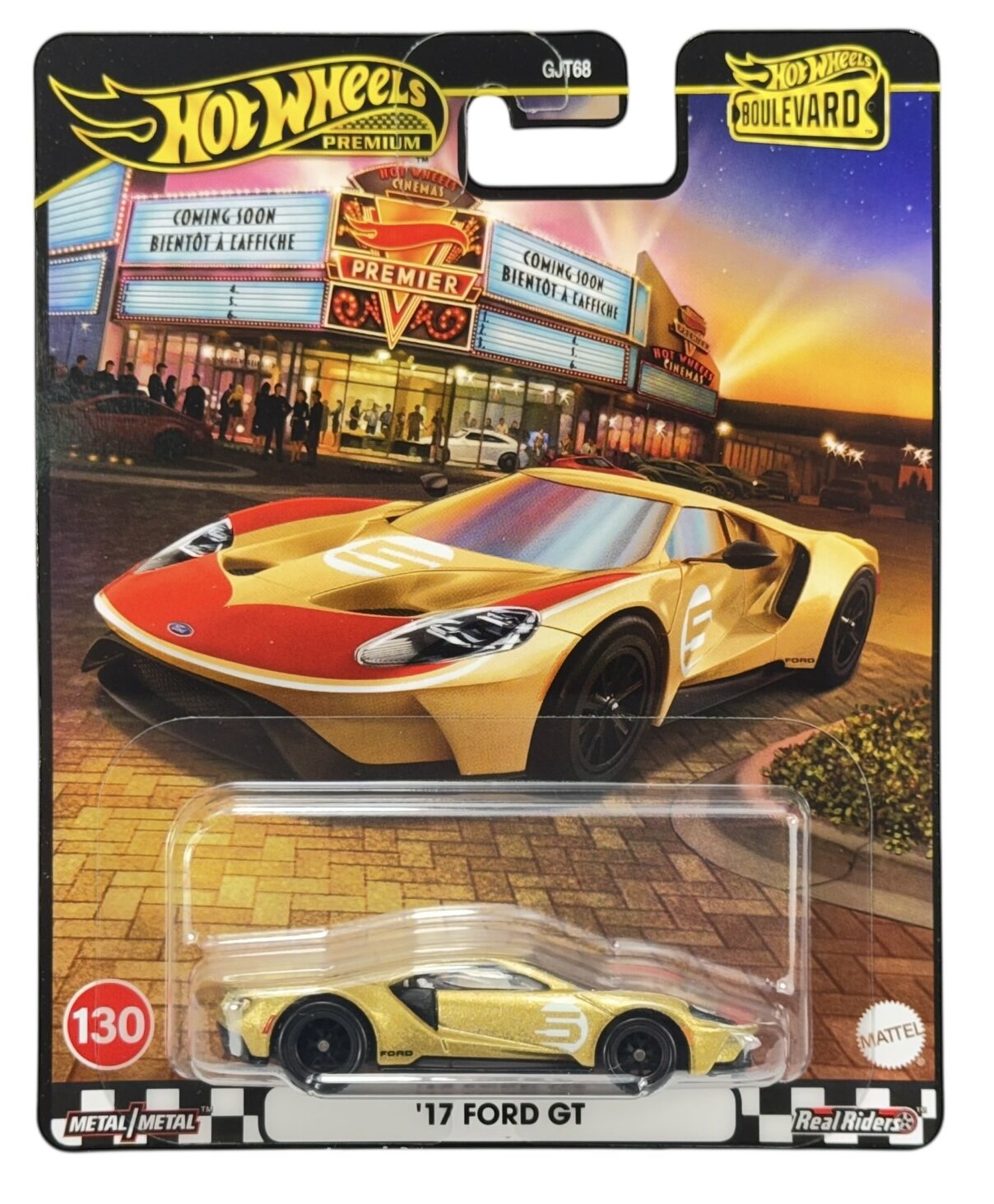 Opakowanie z modelem samochodu \'17 Ford GT w kolorze złotym z numerem 5 na boku. W tle widoczny jest budynek kina z napisami \'COMING SOON BIENTOT A L\'AFFICHE\'.