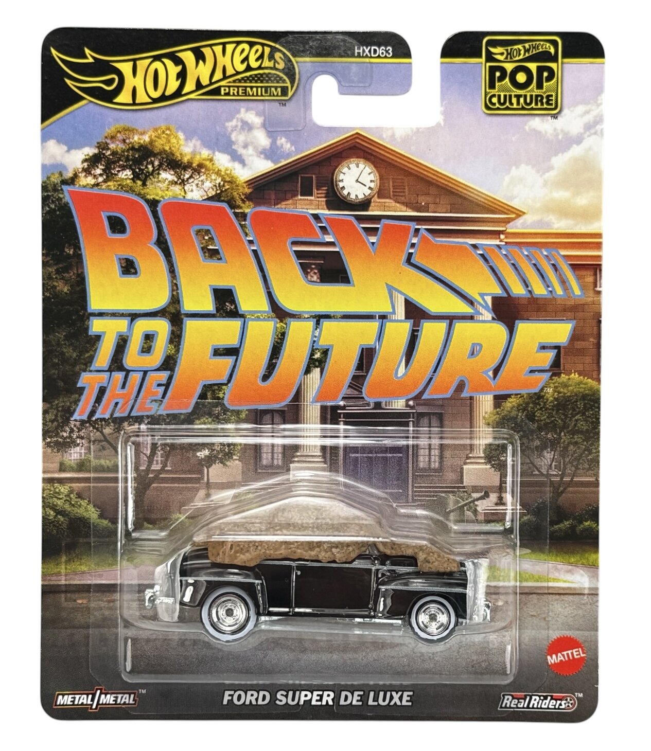Opakowanie modelu samochodu Hot Wheels Premium z serii Pop Culture, przedstawiające Ford Super De Luxe na tle budynku z zegarem. Widoczny jest napis \'BACK TO THE FUTURE\' oraz logo Mattel.