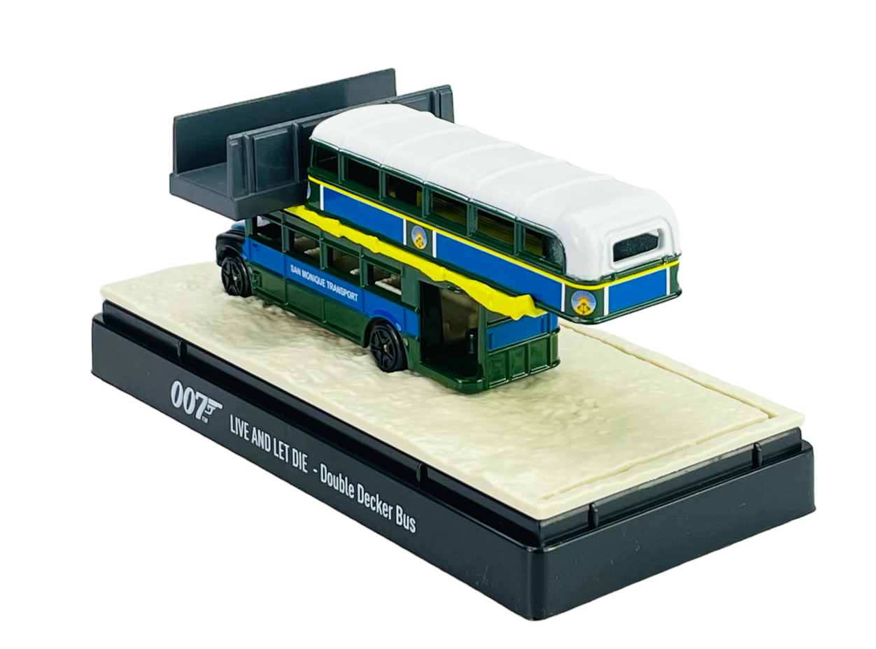 Model metalowego autobusu piętrowego w kolorach niebieskim, zielonym i białym, umieszczony na podstawce z napisem \'007 LIVE AND LET DIE - Double Decker Bus\'.