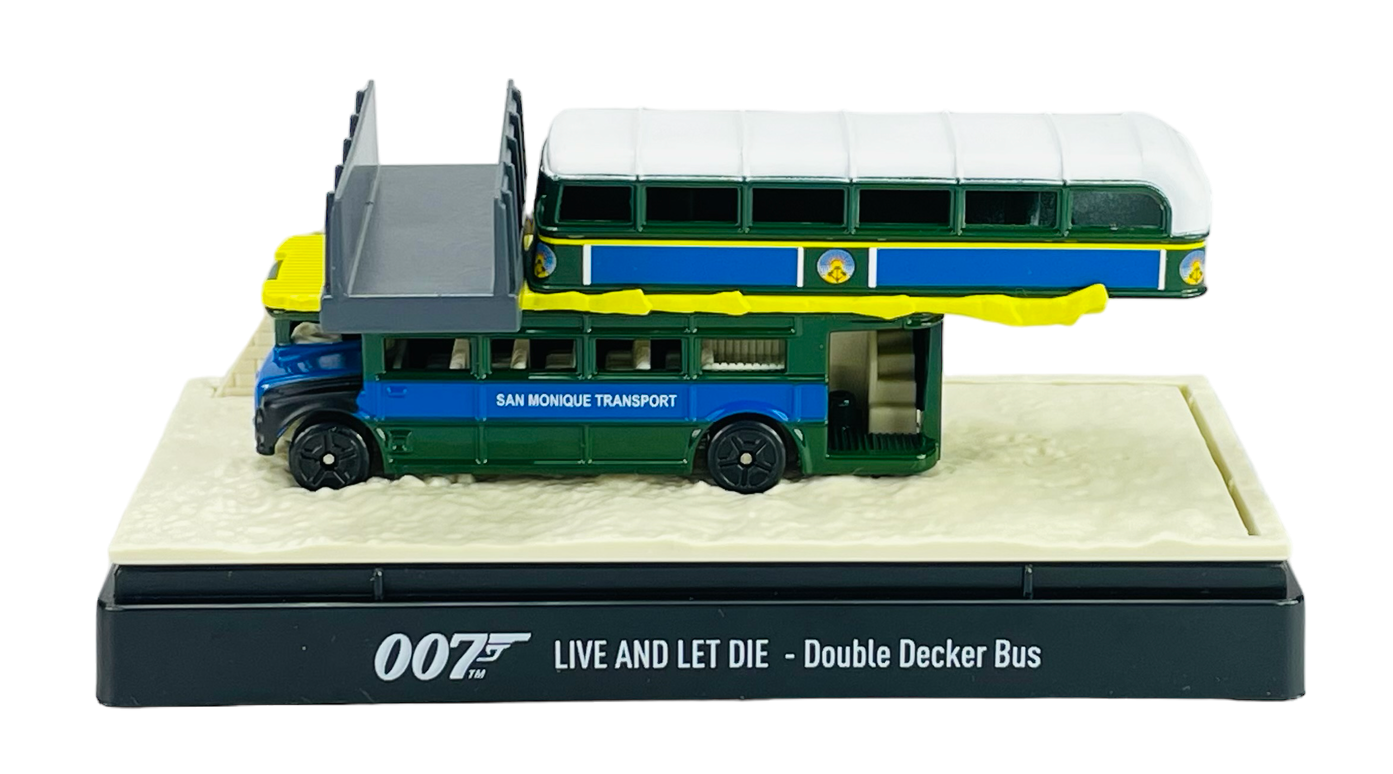 Model autobusu piętrowego w kolorach zielonym i niebieskim z napisem \'SAN MONIQUE TRANSPORT\' na boku, umieszczony na podstawce z napisem \'007 LIVE AND LET DIE - Double Decker Bus\'.