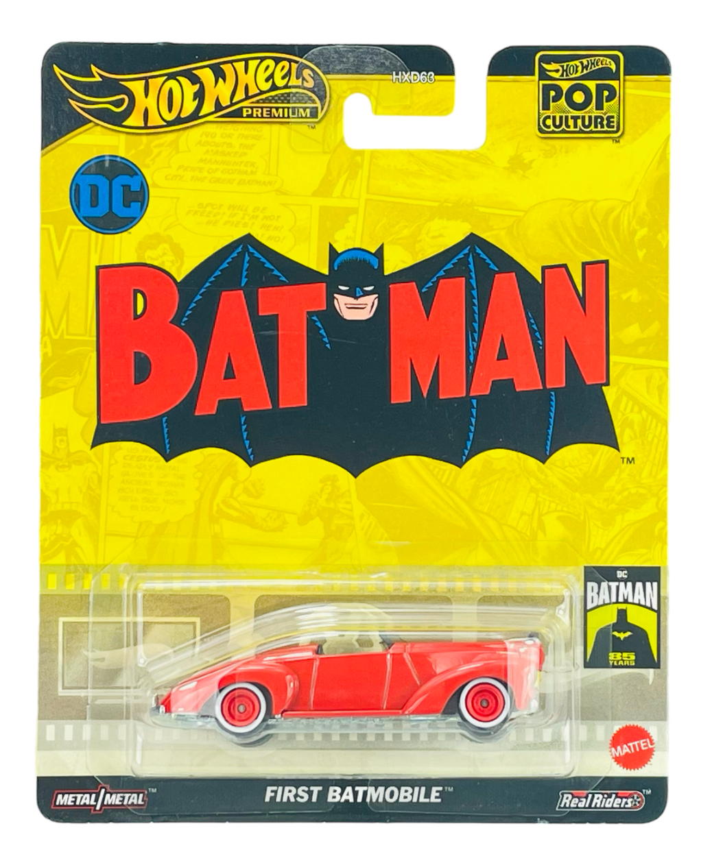 Opakowanie z modelem samochodu Hot Wheels Premium z serii Pop Culture, przedstawiające czerwony pojazd \'First Batmobile\'. Na opakowaniu widoczne są napisy \'BATMAN\', \'DC\', \'Metal/Metal\', \'Real Riders\' oraz logo \'Mattel\'.