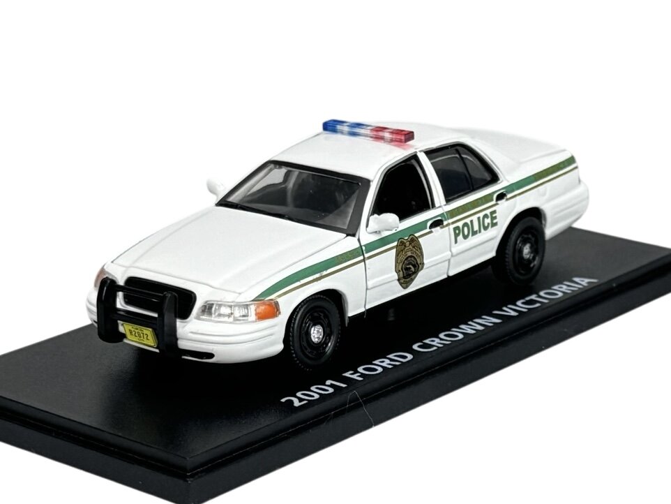 Model policyjnego samochodu Ford Crown Victoria z 2001 roku w kolorze białym z zielonymi detalami i napisem \'POLICE\'. Pojazd umieszczony jest na podstawce z napisem \'2001 FORD CROWN VICTORIA\'.