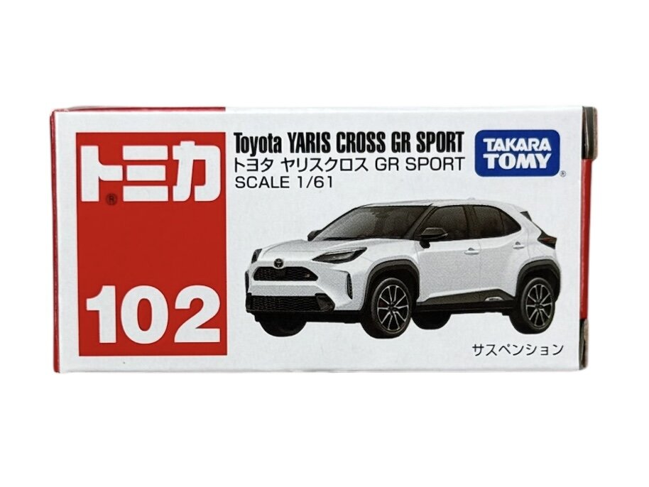 Opakowanie modelu samochodu z napisem \'Toyota YARIS CROSS GR SPORT SCALE 1/61\' oraz logo \'TAKARA TOMY\'. Widoczny jest biały model samochodu i czerwony numer \'102\'.