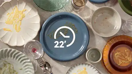 Na obrazie widoczne są różnokolorowe talerze i szklanki z resztkami jedzenia, a na niebieskim talerzu znajduje się symbol zegara z napisem \'22\'.