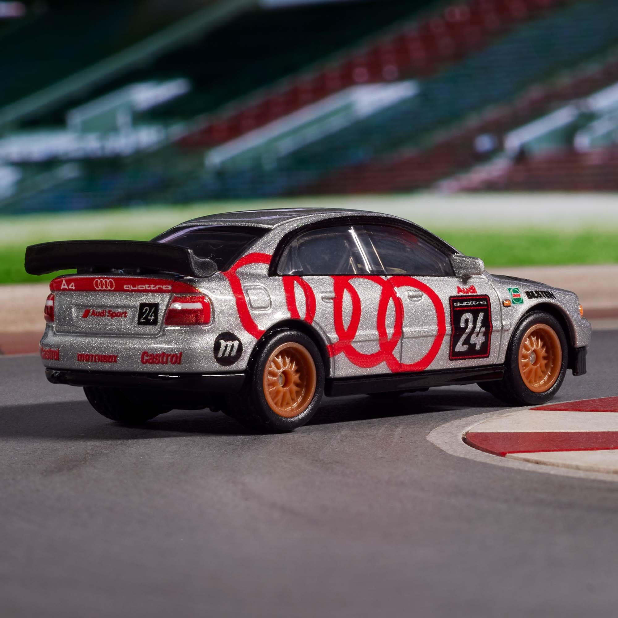 Model samochodu wyścigowego w srebrnym kolorze z czerwonymi i czarnymi oznaczeniami, w tym logo Audi i numerem 24. Na samochodzie widoczne są napisy: \'A4\', \'quattro\', \'Audi Sport\', \'Castrol\'.