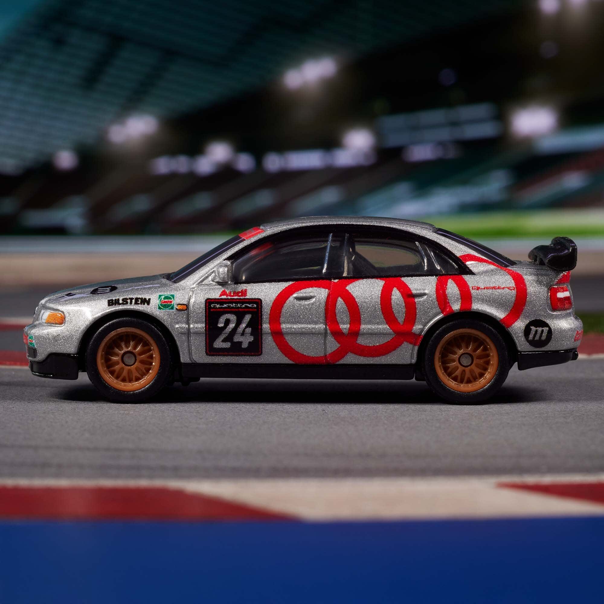 Model samochodu wyścigowego w srebrnym kolorze z czerwonymi pierścieniami i numerem 24 na boku. Na karoserii widoczne są logotypy \'Audi\', \'Bilstein\' oraz inne oznaczenia wyścigowe.