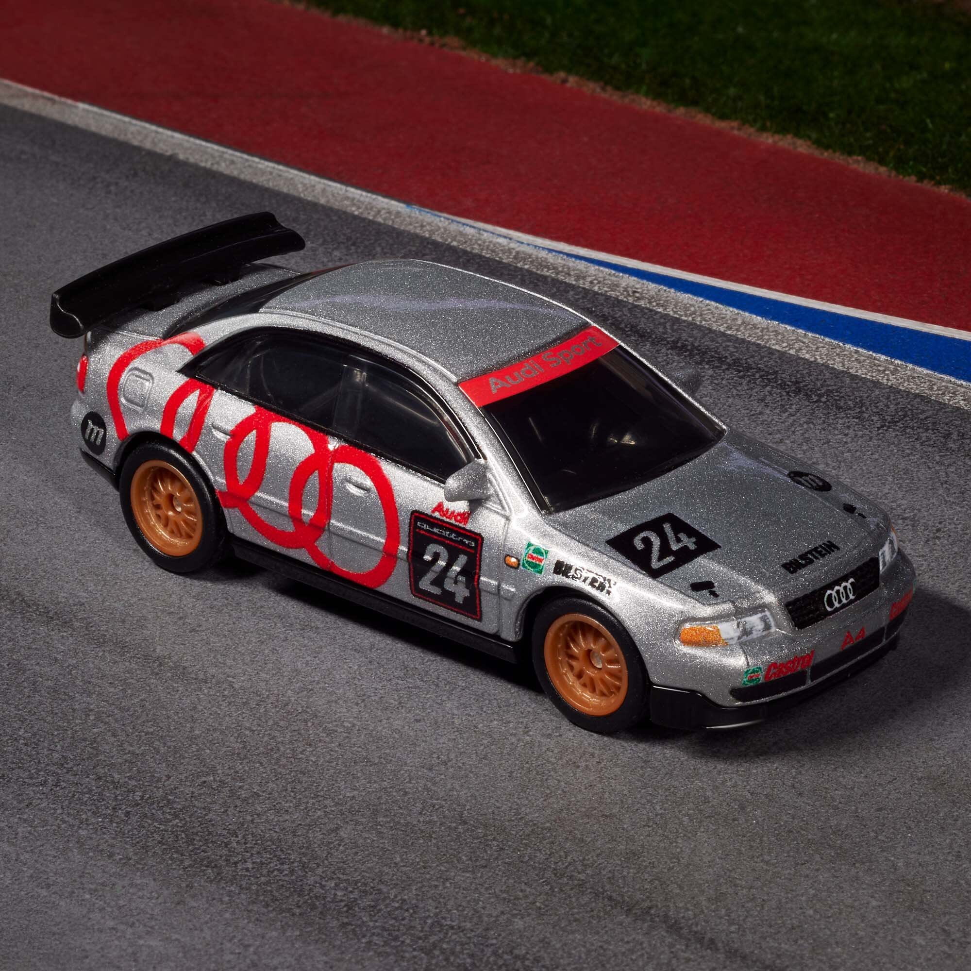 Model samochodu wyścigowego w srebrnym kolorze z czerwonymi i czarnymi detalami, oznaczony numerem 24. Na masce widoczne jest logo Audi oraz napisy \'Audi Sport\' i \'Bilstein\'.