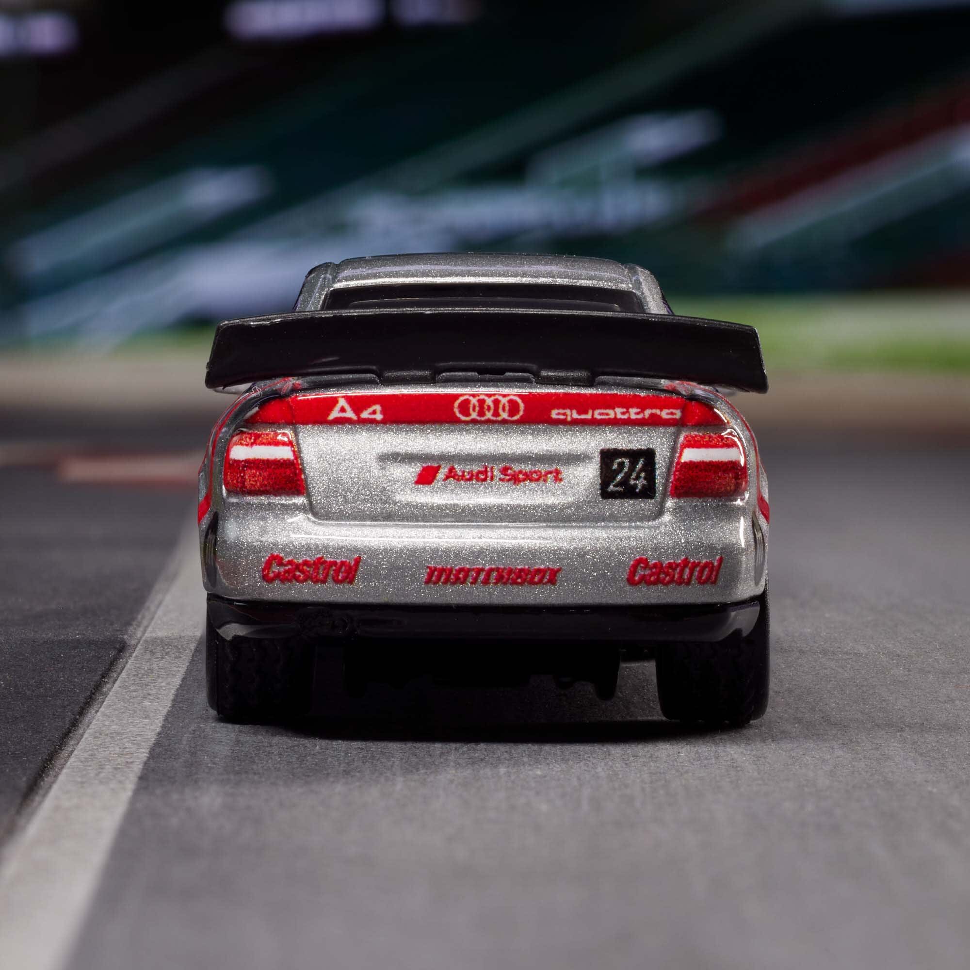 Model samochodu wyścigowego z widocznymi napisami: \'A4\', \'Audi Sport\', \'quattro\', \'Castrol\', \'24\'. Samochód jest srebrny z czerwonymi detalami i dużym tylnym spojlerem.