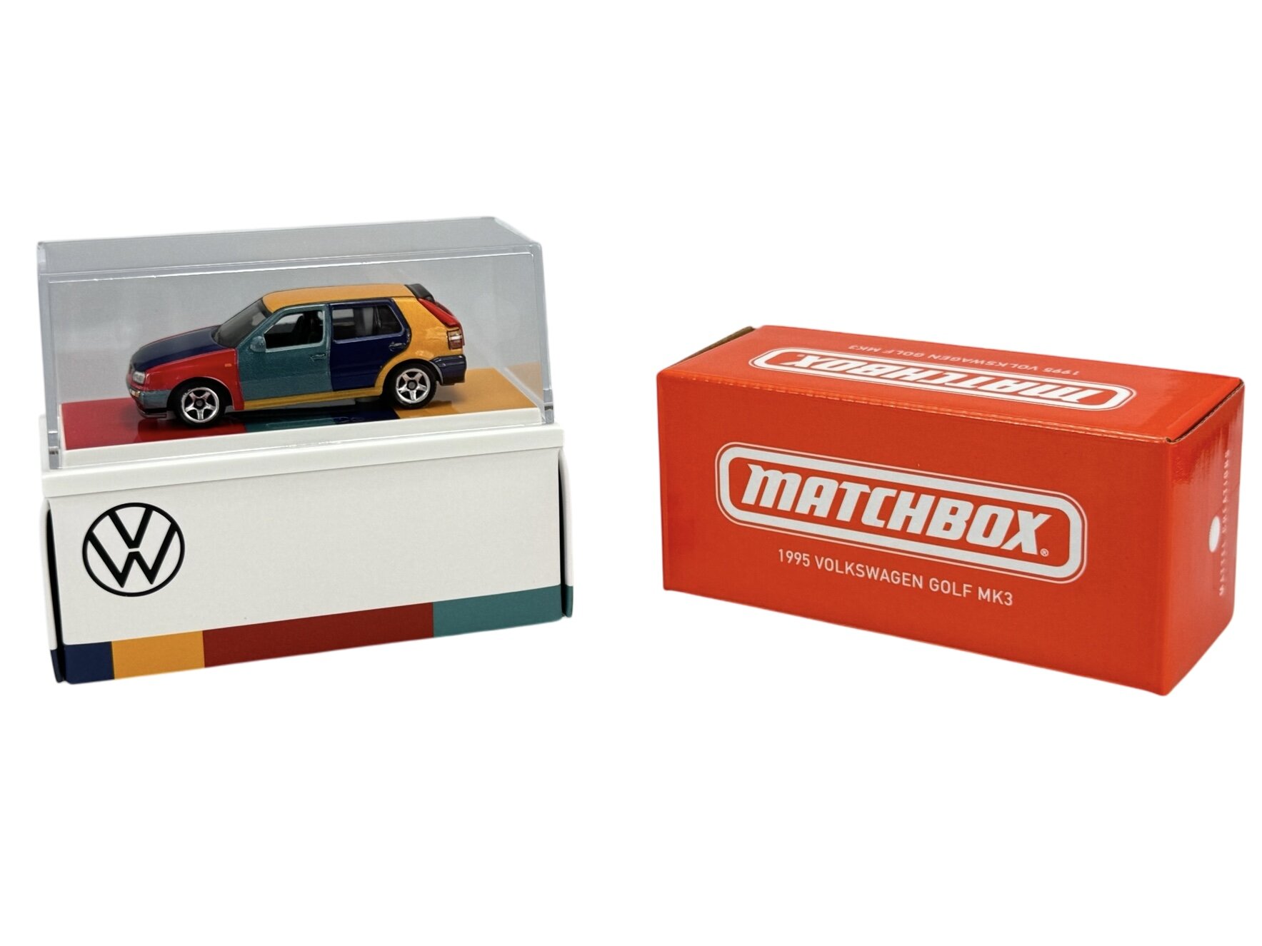 Model samochodu w kolorach harlekinowych znajduje się w przezroczystej gablocie na podstawce z logo VW. Obok stoi pomarańczowe pudełko z napisem \'MATCHBOX 1995 VOLKSWAGEN GOLF MK3\'.