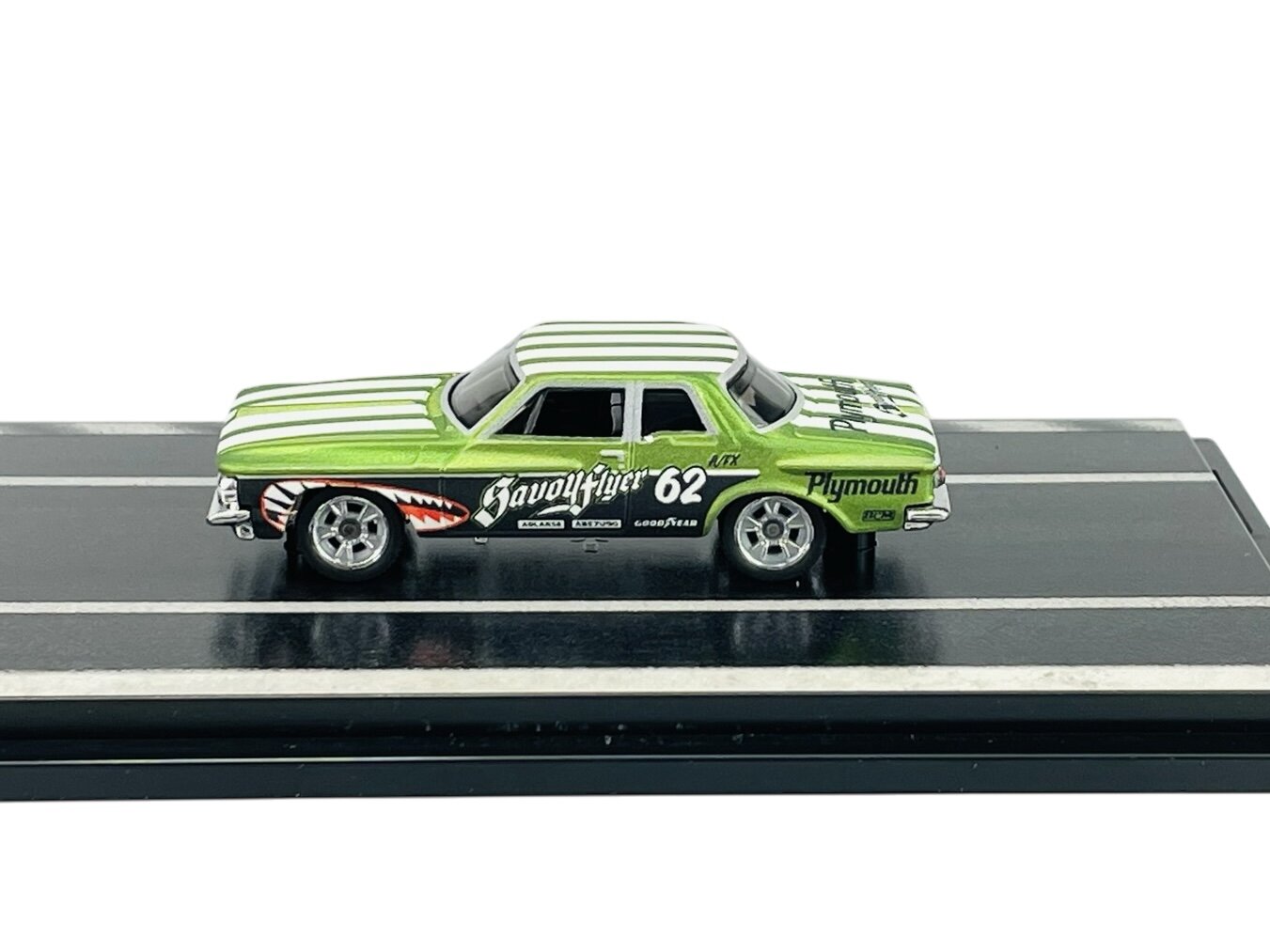 Model samochodu w kolorze zielonym z białymi pasami, umieszczony na czarnej podstawce. Na boku widoczne napisy: \'Savoy Flyer 62\', \'Plymouth\', \'Goodyear\'.