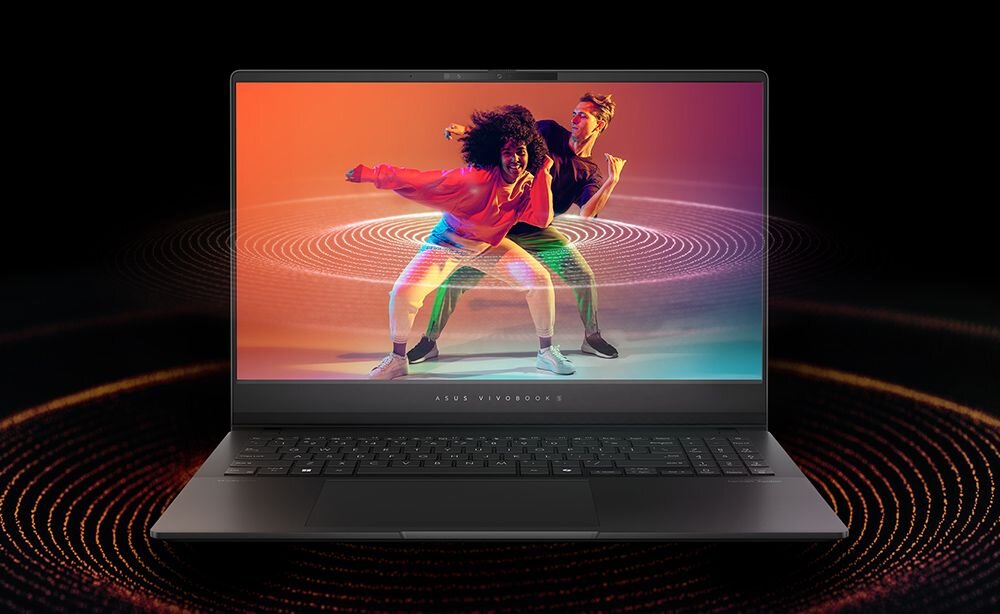 Laptop z wyświetlaczem pokazującym dwie osoby tańczące na kolorowym tle. Na obudowie widoczny jest napis \'ASUS VIVOBOOK\'.