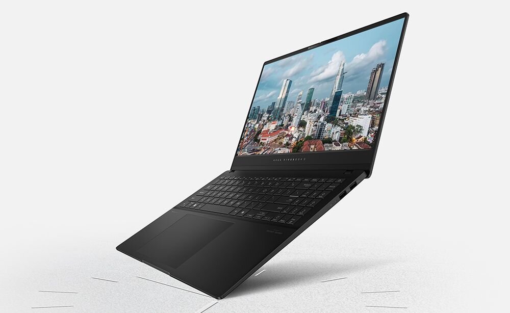 Laptop z otwartym ekranem, na którym wyświetlany jest obraz miasta z wieżowcami. Klawiatura jest widoczna, a obudowa ma ciemny kolor.