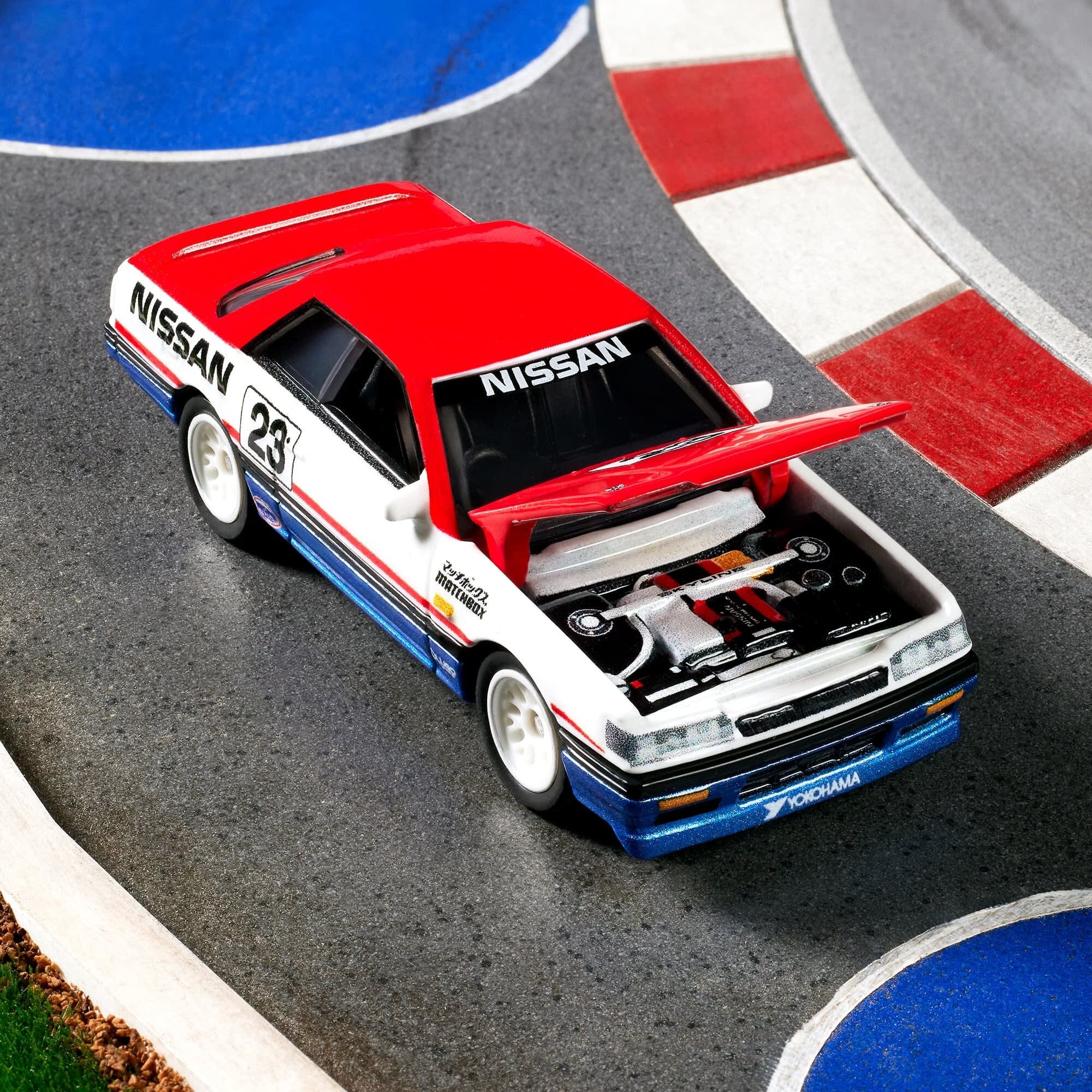 Model samochodu wyścigowego z otwartą maską, w kolorach czerwonym, białym i niebieskim, z widocznymi napisami \'NISSAN\' i \'YOKOHAMA\'. Samochód znajduje się na torze wyścigowym z czerwono-białymi i niebieskimi oznaczeniami.