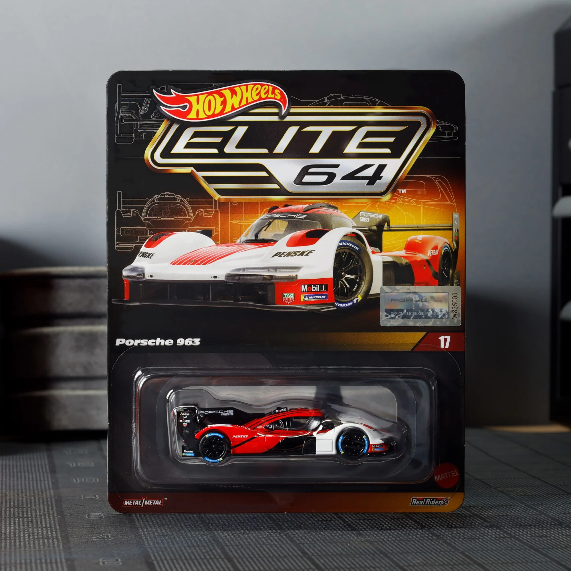 Opakowanie modelu samochodu Hot Wheels Elite 64 z widocznym modelem Porsche 963 w kolorach białym, czerwonym i czarnym. Na opakowaniu znajduje się logo Hot Wheels oraz napis \'Porsche 963\'.