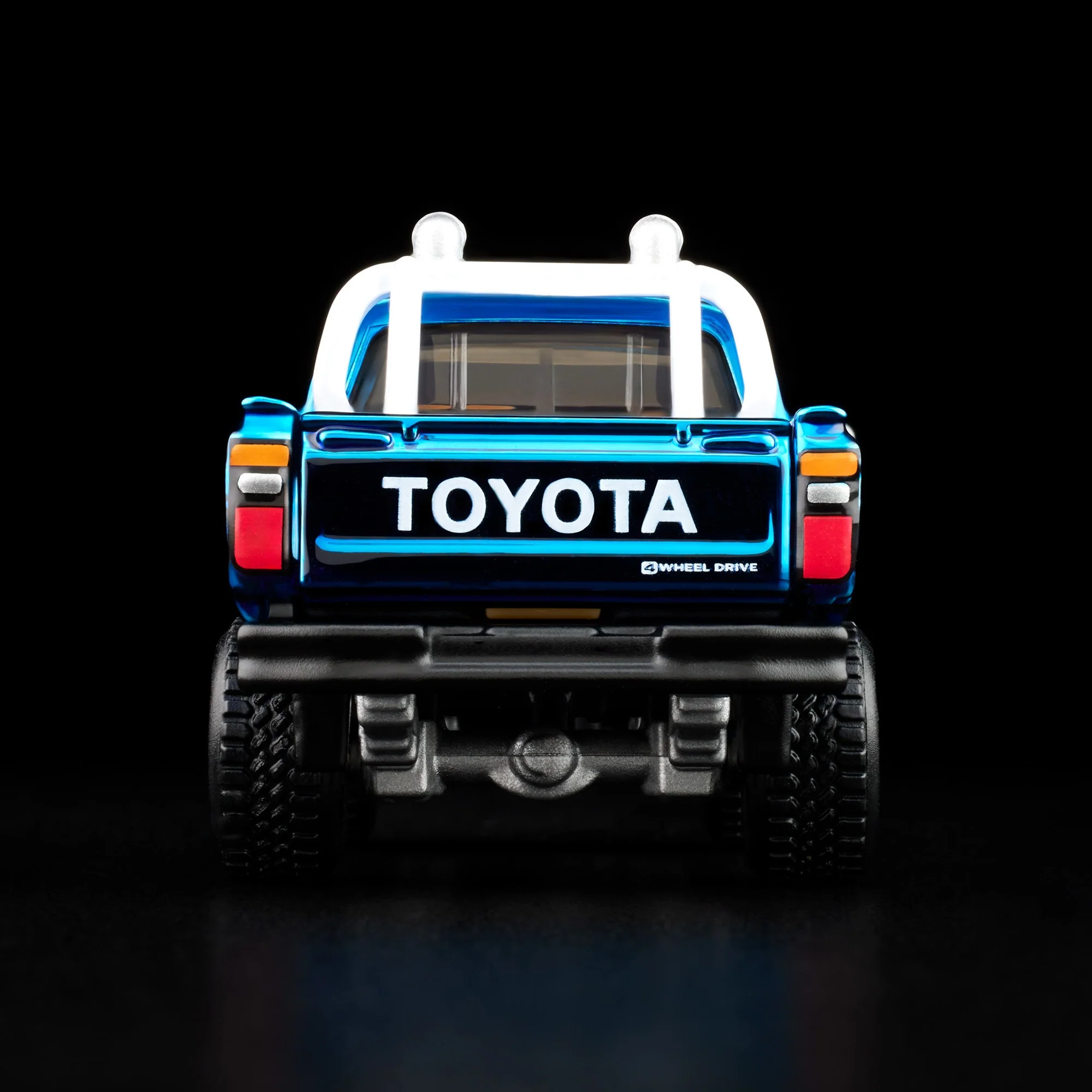 Model samochodu terenowego z napisem \'TOYOTA\' na tylnej klapie, w kolorze niebieskim z białymi i czerwonymi akcentami. Widoczne są duże opony i napis \'4 WHEEL DRIVE\'.
