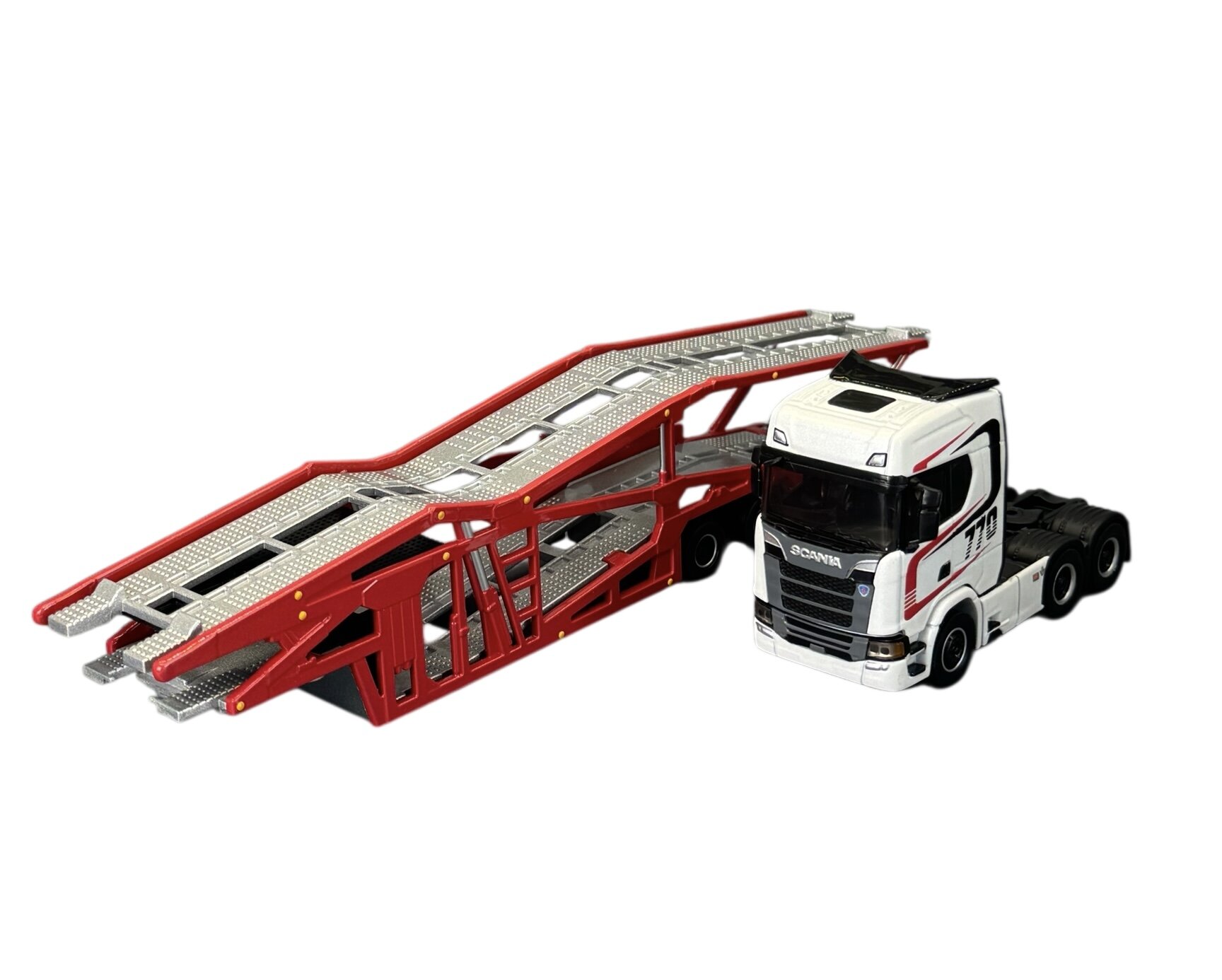 Model metalowy ciężarówki z naczepą do przewozu samochodów, w kolorze białym z czarnymi i czerwonymi detalami. Na kabinie widoczny napis \'Scania\'.