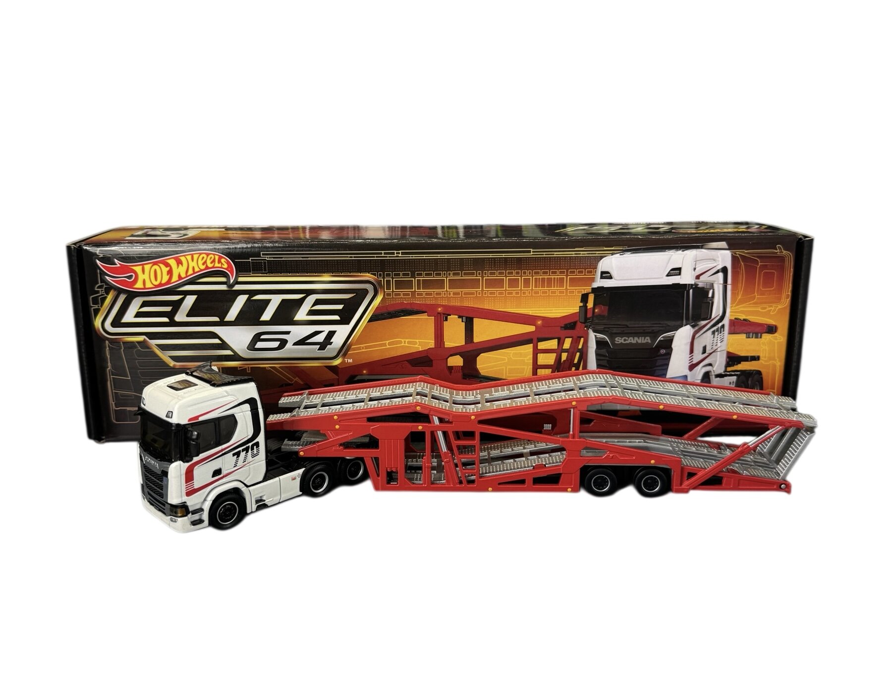 Model ciężarówki w skali 1:64 z napisem \'770\' na boku, w kolorze białym z czerwonymi elementami, stoi przed pudełkiem z logo \'Hot Wheels Elite 64\'.