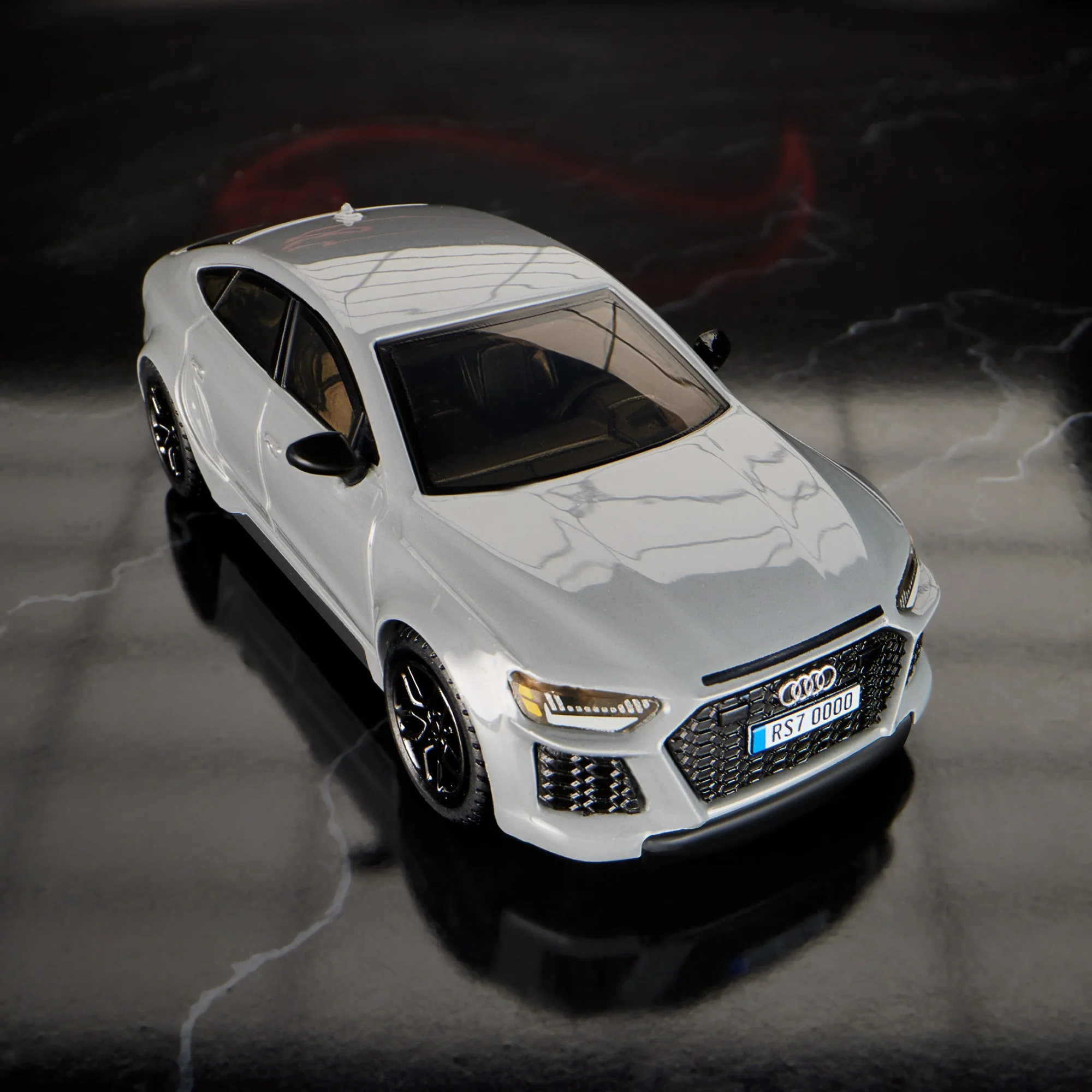 Model samochodu w kolorze srebrnym z widocznym logo Audi na grillu. Tablica rejestracyjna z napisem \'RS7 0000\'.