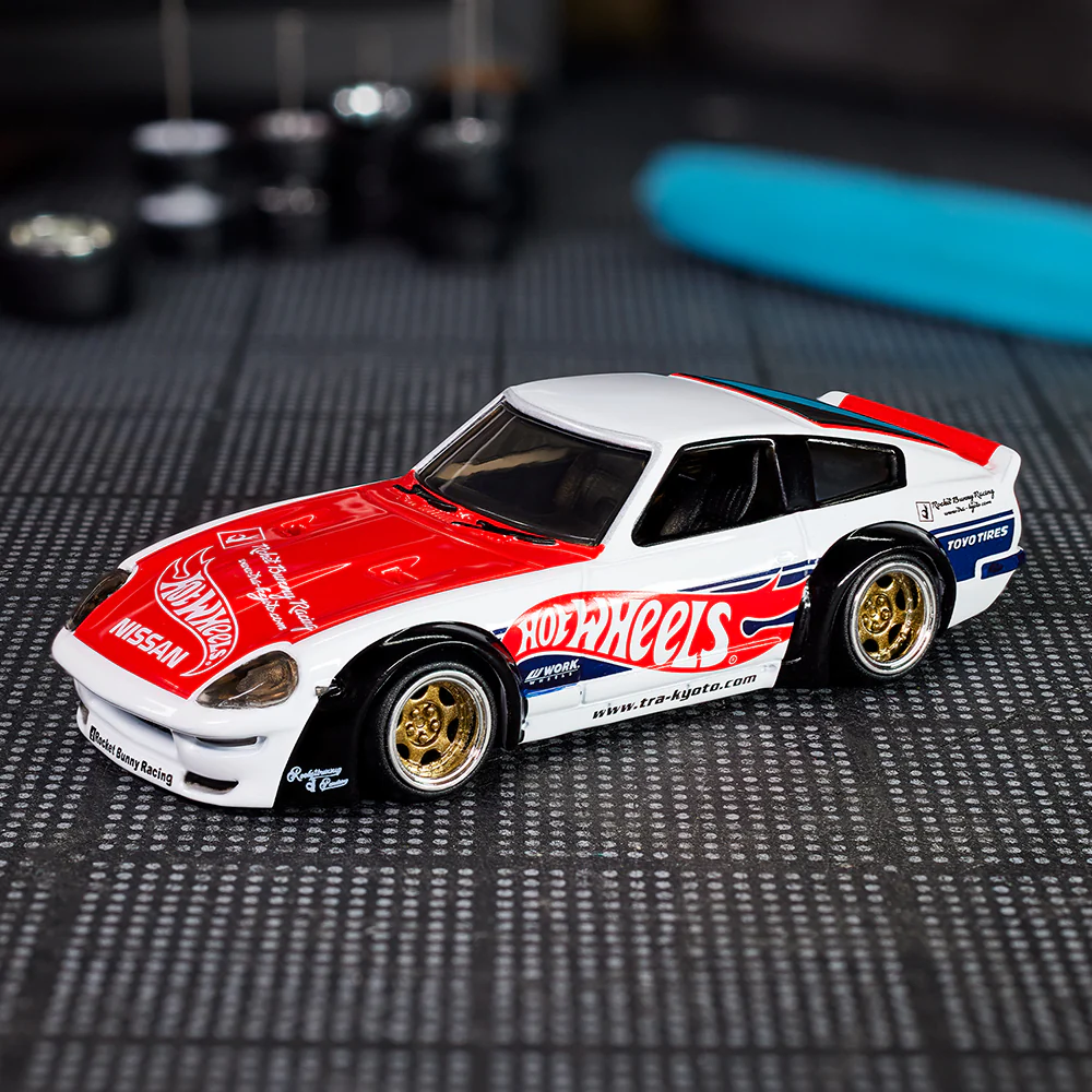 Model samochodu Hot Wheels z czerwono-białym nadwoziem i złotymi felgami. Na karoserii widoczne są napisy \'Hot Wheels\', \'Nissan\' oraz \'Toyo Tires\'.