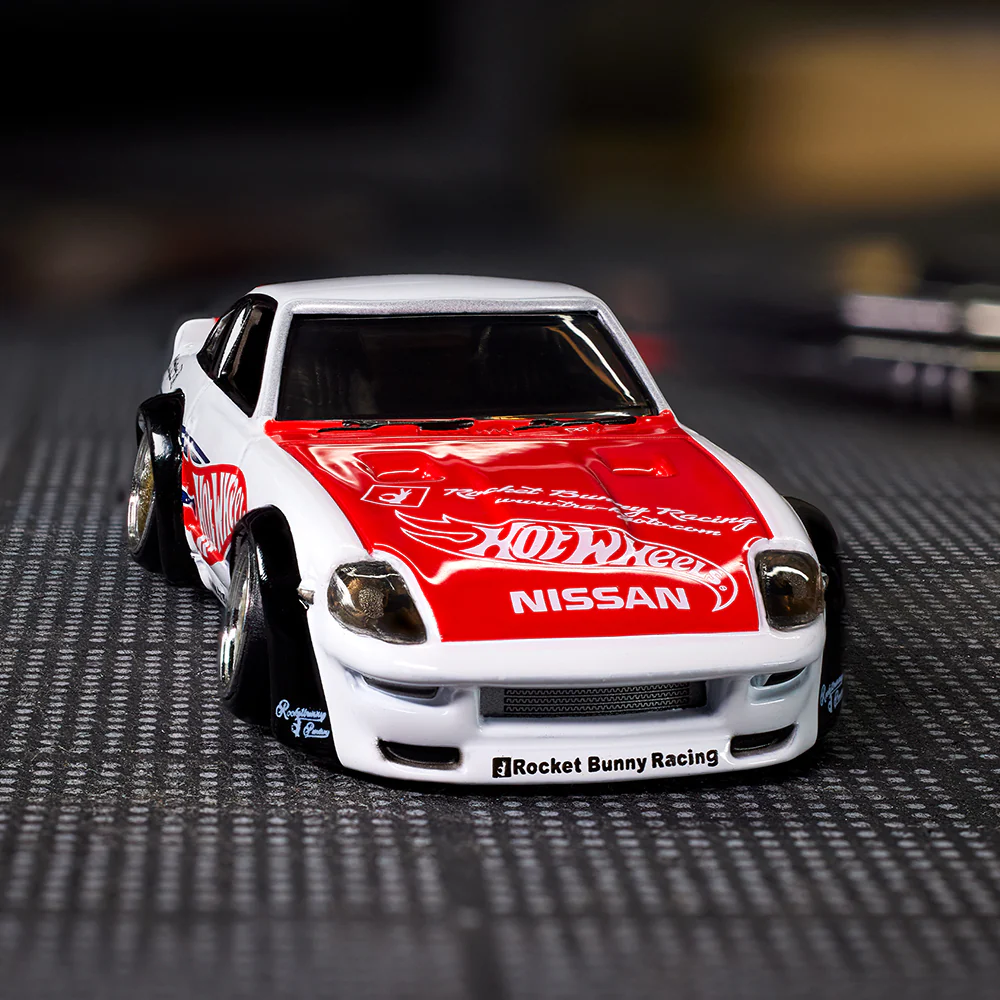 Model samochodu z białym nadwoziem i czerwonymi akcentami, z widocznymi napisami \'Hot Wheels\', \'NISSAN\' i \'Rocket Bunny Racing\'.