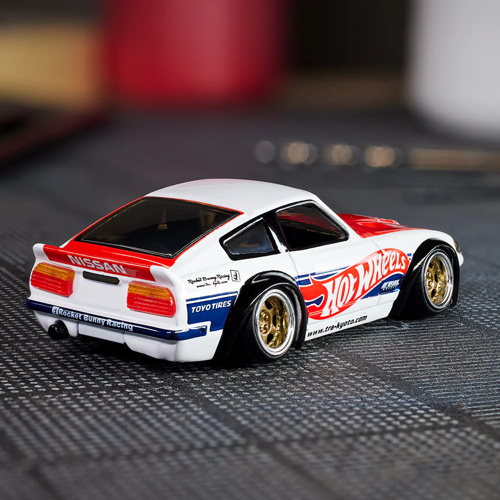 Model samochodu w kolorach białym, czerwonym i niebieskim z logo \'Hot Wheels\' na boku. Na tylnej części widoczne napisy: \'NISSAN\', \'Rocket Bunny Racing\', \'TOYO TIRES\'.