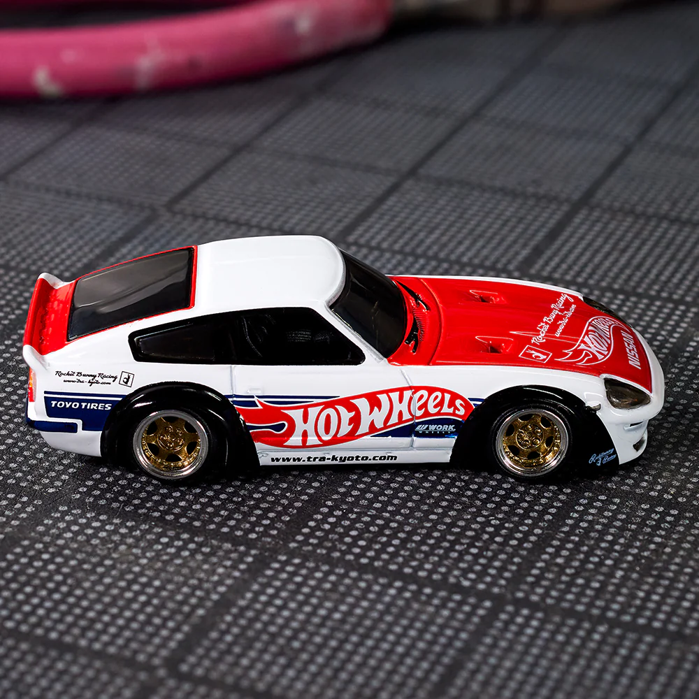 Model samochodu w kolorach czerwonym i białym z logo \'Hot Wheels\' na boku. Na oponach widoczny napis \'TOYO TIRES\'.