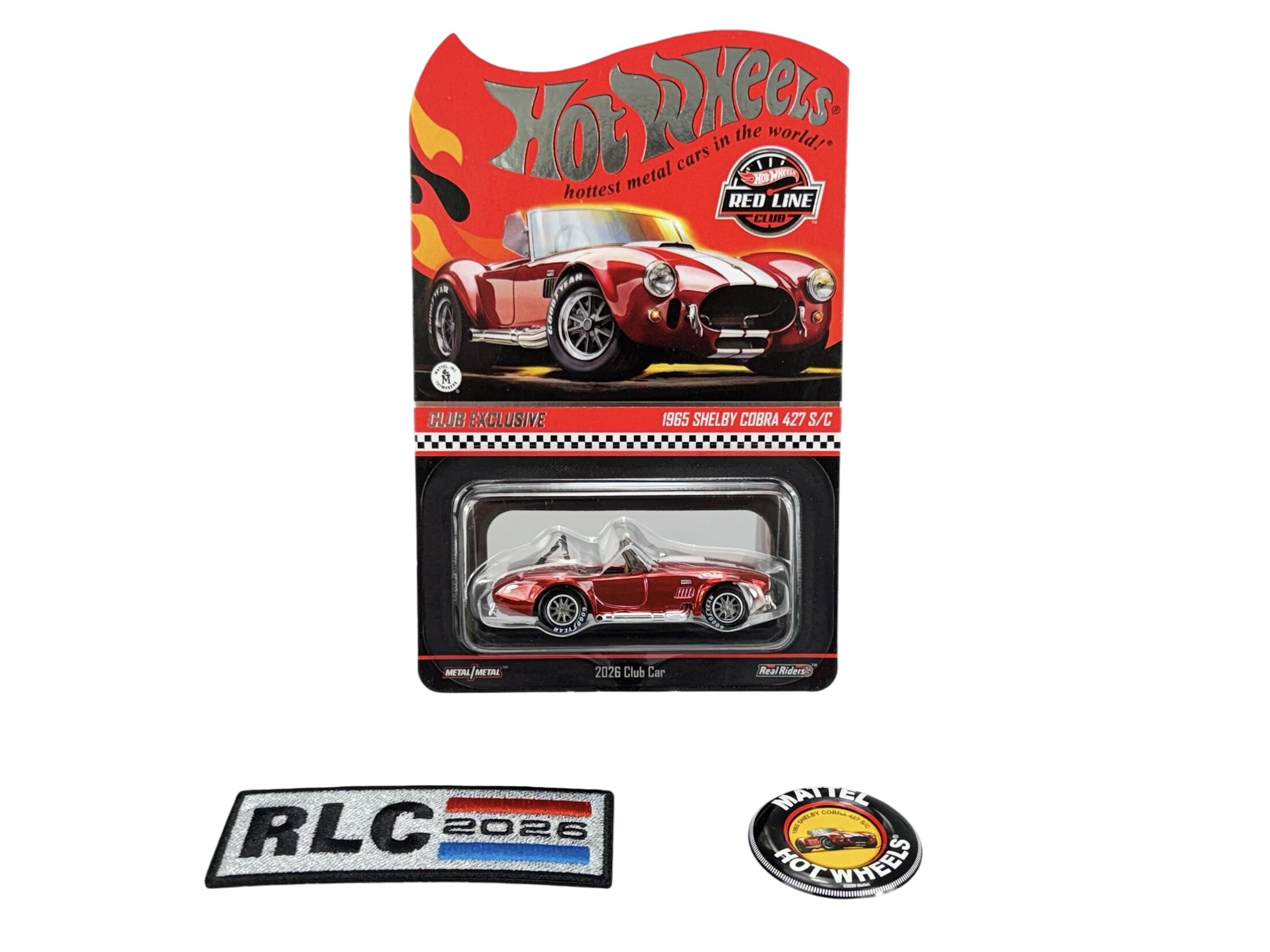Opakowanie modelu samochodu Hot Wheels z czerwonym pojazdem 1965 Shelby Cobra 427 S/C, z widocznym logo \'Red Line Club\'. Obok znajdują się naszywka z napisem \'RLC 2026\' oraz okrągła naszywka z logo Hot Wheels.