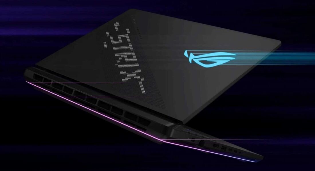 Laptop z podświetlanym logo i wzorem na obudowie, widoczny z boku. Obudowa ma ciemny kolor z elementami świetlnymi w odcieniach niebieskiego i fioletowego.