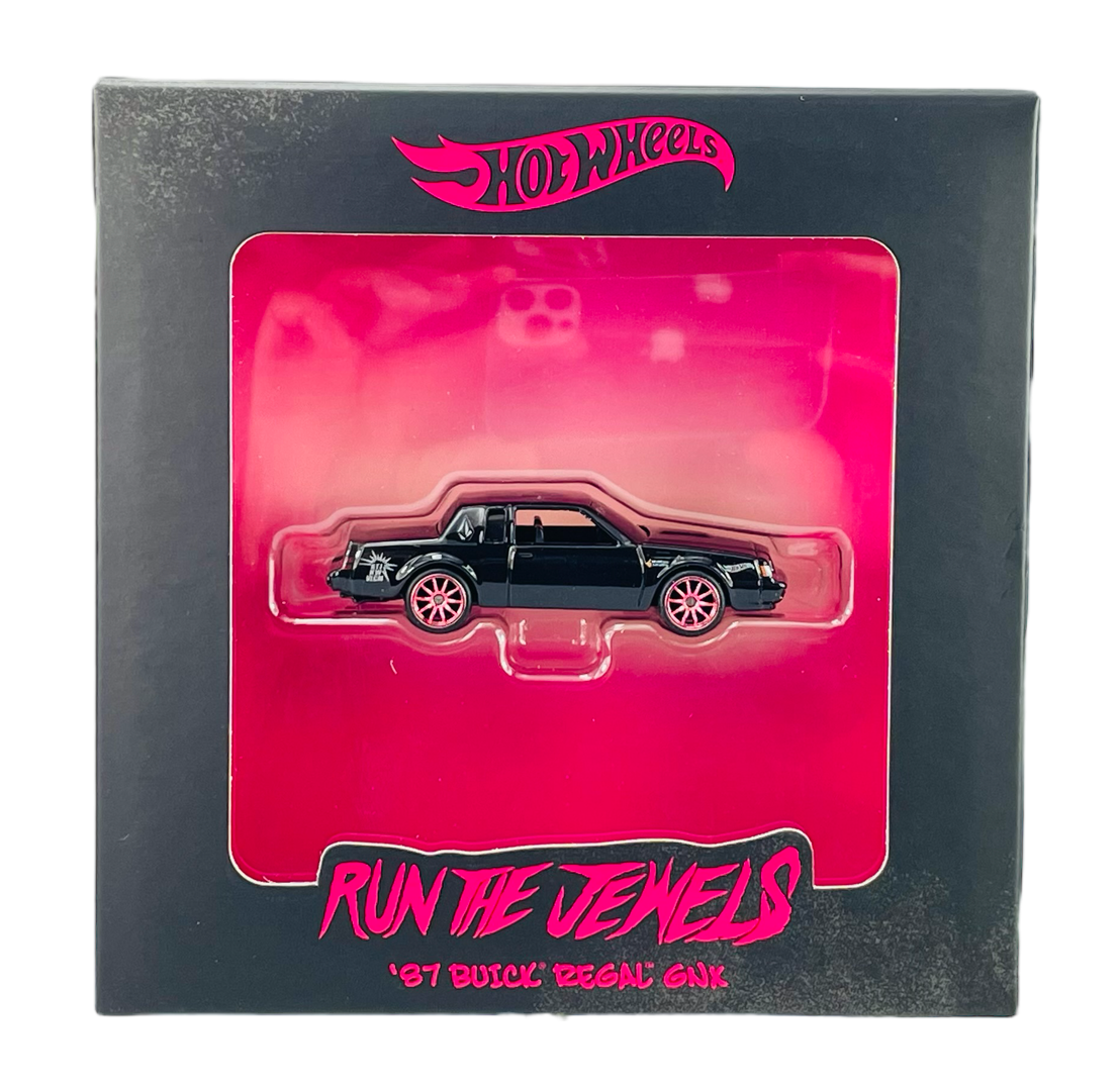 Opakowanie z modelem samochodu w kolorze czarnym, z różowymi felgami, umieszczonym na różowym tle. Na opakowaniu widoczne są napisy: \'Hot Wheels\', \'Run The Jewels\', \'\'87 Buick Regal GNX\'.