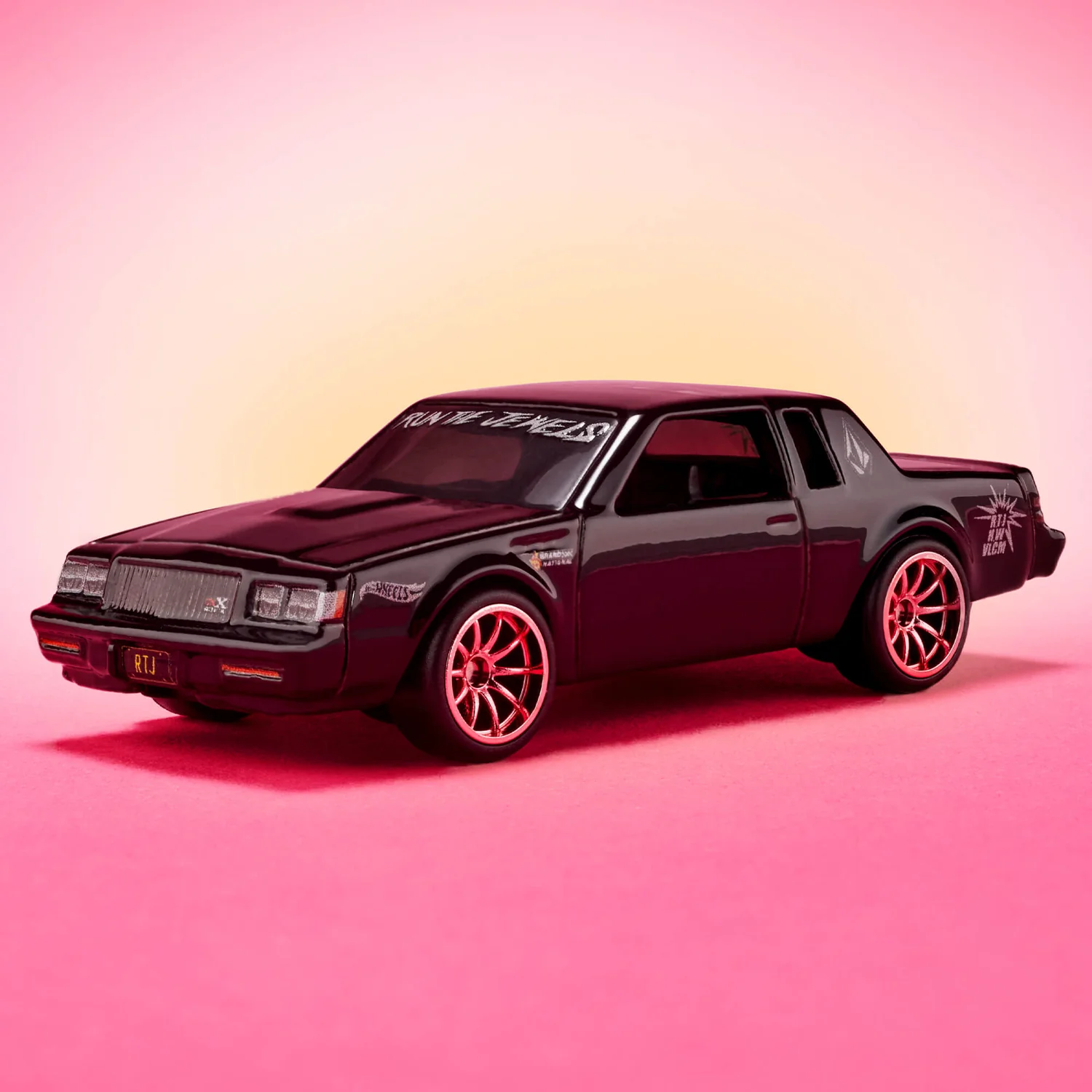 Model samochodu w kolorze czarnym z napisem \'RUN THE JEWELS\' na przedniej szybie, ustawiony na różowym tle. Na boku widoczne logo \'Hot Wheels\' oraz napis \'RTJ x VOLCOM\'.