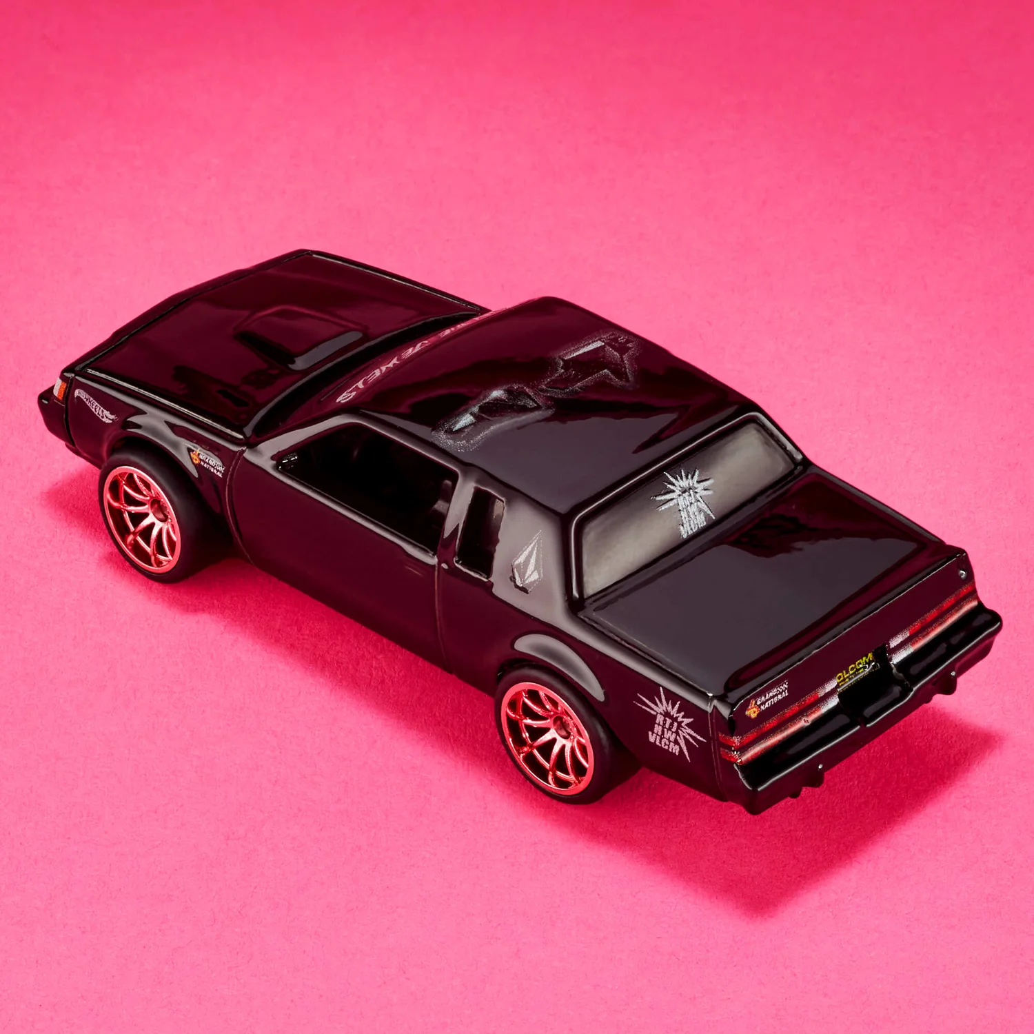 Czarny model samochodu z czerwonymi felgami na różowym tle, z widocznymi białymi grafikami i napisami na karoserii. Na tylnej szybie znajduje się napis \'RUN THE JEWELS\'.