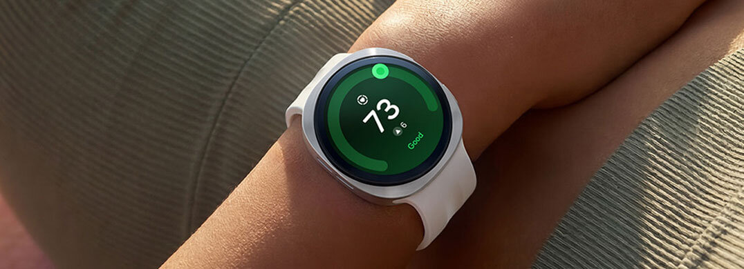 Na zdjęciu widać smartwatch z okrągłym wyświetlaczem, na którym widnieje liczba 73 oraz napis \'Good\'. Urządzenie ma jasny pasek i jest noszone na nadgarstku.