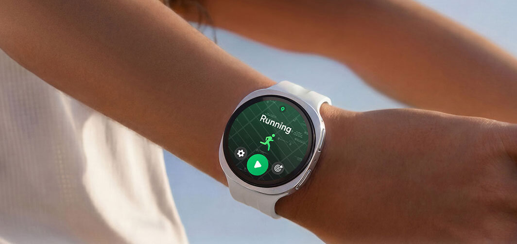 Osoba nosi smartwatch z białym paskiem, na ekranie widoczna jest aplikacja do biegania z napisem \'Running\'.