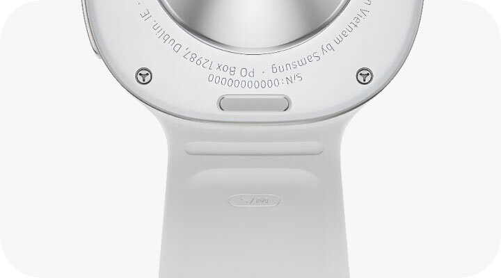 Zbliżenie na tylną część smartwatcha z widocznym napisem \'Designed by Samsung\' oraz numerem seryjnym \'S/N: 000000000000\'. Pasek zegarka jest w jasnym kolorze.