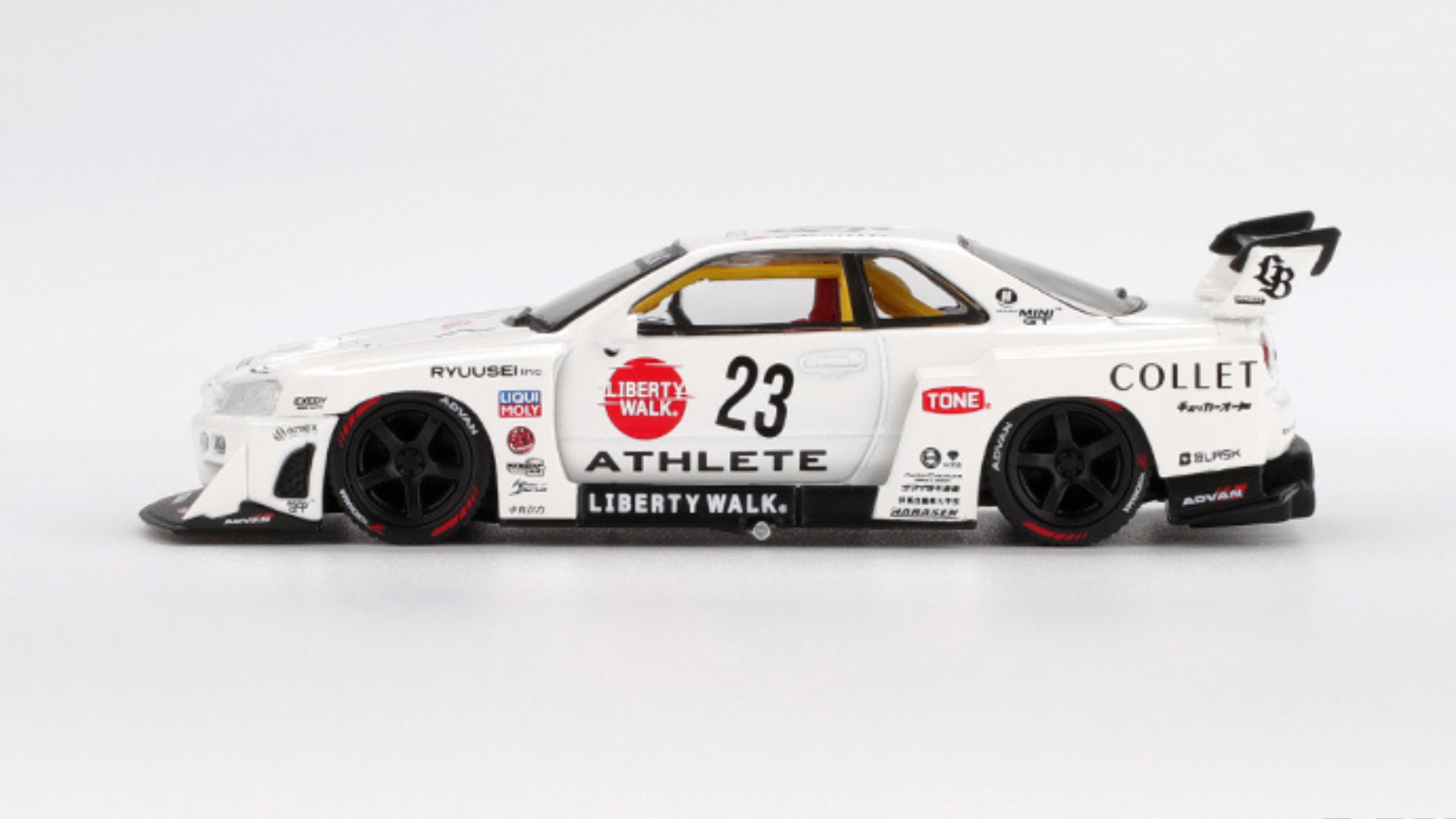 Model samochodu wyścigowego w skali 1:64, biały z czarnymi detalami i numerem 23 na drzwiach. Na karoserii widoczne są logotypy, w tym \'Liberty Walk\', \'Athlete\' oraz inne oznaczenia sponsorów.