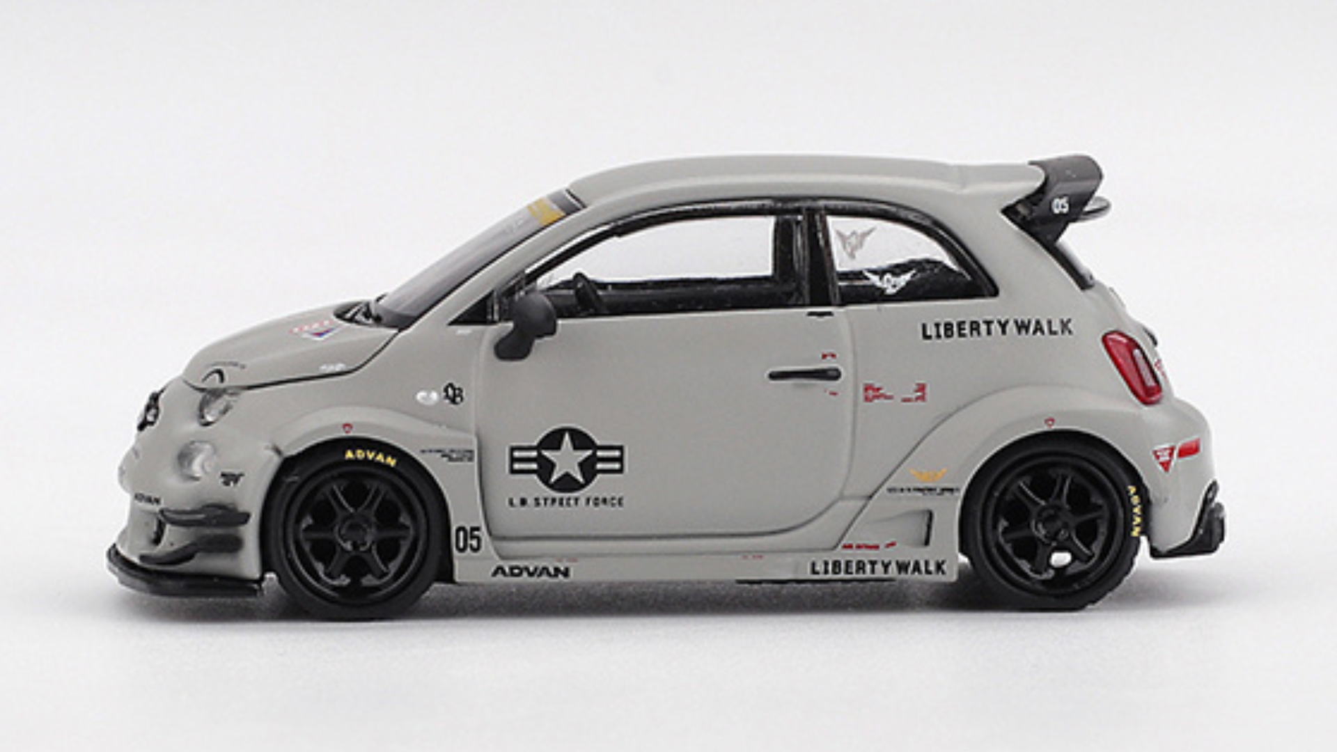 Model samochodu w kolorze szarym z czarnymi kołami, ozdobiony napisami \'LIBERTY WALK\' i \'L.B. STREET FORCE\'. Na boku widoczne są również inne oznaczenia i symbole, w tym logo z gwiazdą i skrzydłami.