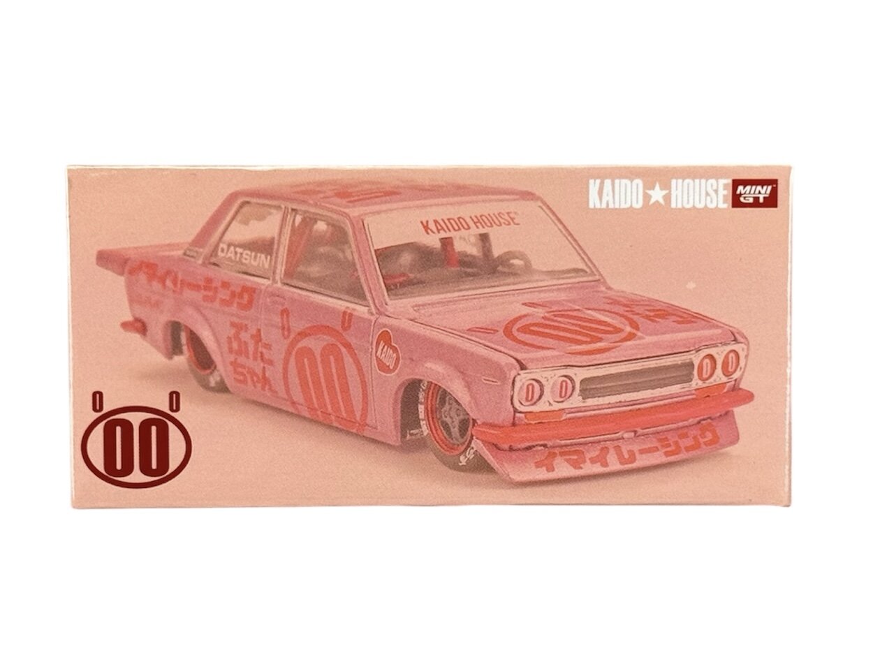 Obraz przedstawia model samochodu Datsun 510 w różowym kolorze z napisami \'KAIDO HOUSE\' i \'MINI GT\' na opakowaniu. Na samochodzie widoczne są czerwone wzory i napisy w języku japońskim.