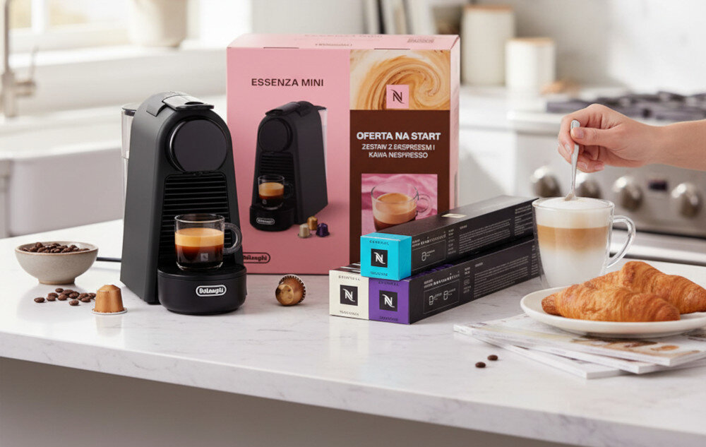 Na blacie kuchennym znajduje się czarny ekspres do kawy z filiżanką espresso, obok pudełko z napisem \'ESSENZA MINI\' i \'OFERTA NA START ZESTAW Z EKSPRESAMI I KAWA NESPRESSO\'. W tle widoczne są kapsułki kawy, filiżanka z mleczną kawą oraz talerz z rogalikiem.