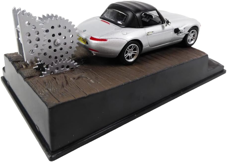 Model samochodu w skali 1:43 przedstawiający srebrny kabriolet z czarnym dachem na podstawce imitującej drewnianą powierzchnię. Obok samochodu znajdują się metalowe koła zębate, a na tablicy rejestracyjnej widnieje napis \'Z8 FMP\'.