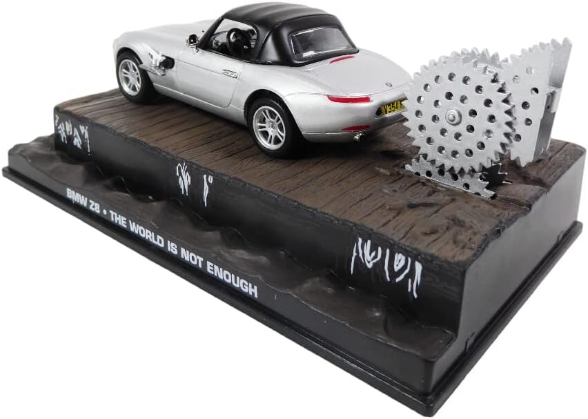 Model samochodu BMW Z8 w skali 1:43 z filmu \'The World Is Not Enough\', umieszczony na podstawce z imitacją drewnianej nawierzchni i metalowym elementem zębatym. Na podstawce widnieje napis \'BMW Z8 - THE WORLD IS NOT ENOUGH\'.