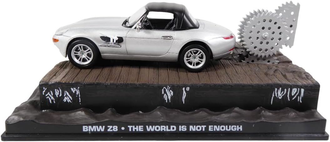 Model samochodu BMW Z8 w kolorze srebrnym, umieszczony na podstawce z napisem \'BMW Z8 • THE WORLD IS NOT ENOUGH\'. Obok samochodu znajduje się duża, zębatkowa piła.