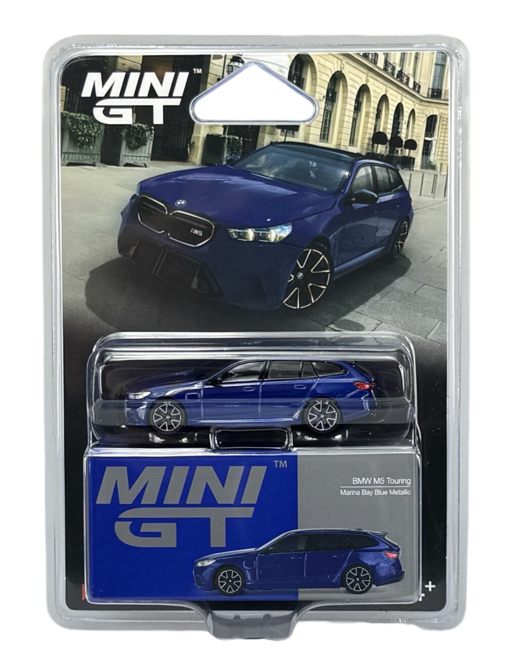 Opakowanie z modelem samochodu Mini GT w kolorze niebieskim, przedstawiające BMW M5 Touring. Na opakowaniu widnieje napis \'MINI GT\' oraz \'BMW M5 Touring Marina Bay Blue Metallic\'.