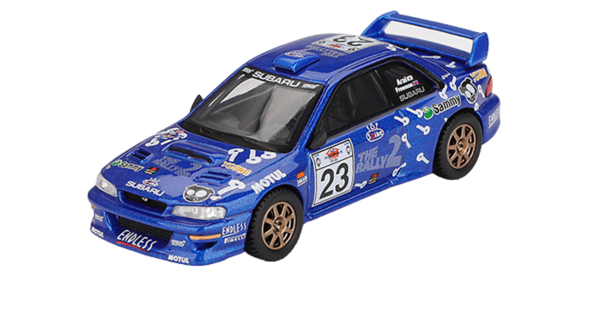 Model samochodu rajdowego w skali 1:64, w kolorze niebieskim z licznymi naklejkami i numerem 23 na drzwiach. Na masce widoczne jest logo \'SUBARU\'.