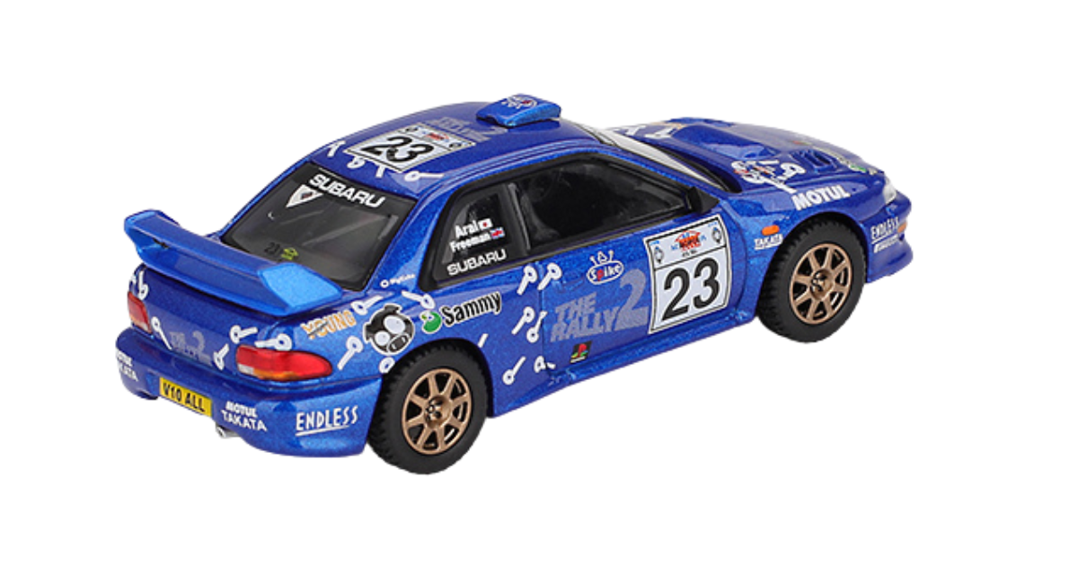 Model samochodu rajdowego w kolorze niebieskim z numerem 23 na drzwiach i dachu. Na karoserii widoczne są liczne logotypy i napisy, w tym \'SUBARU\' i \'THE RALLY\'.