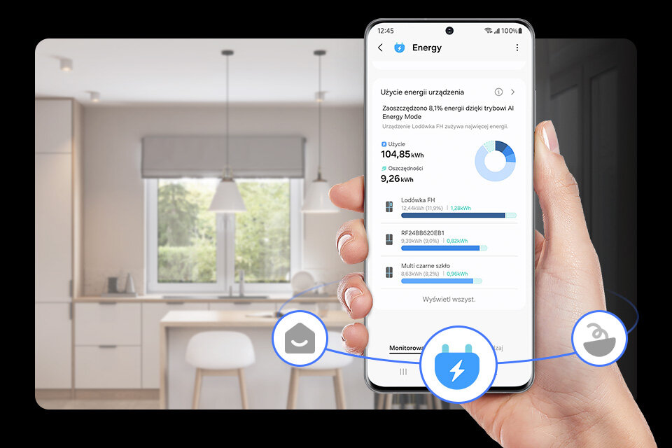 ai energy Osoba trzyma smartfon z aplikacją pokazującą zużycie energii urządzenia, z tekstem: \'Użycie energii urządzenia\', \'Zastosowano 8,1% energii dzięki trybowi AI Energy Mode\', \'Użycie 104,85 kWh\', \'Oszczędności 9,26 kWh\'. W tle widoczna jest nowoczesna kuchnia.