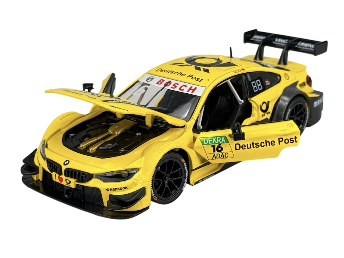 Model samochodu wyścigowego w kolorze żółtym z otwartymi drzwiami i maską, z widocznymi napisami \'Deutsche Post\', \'BOSCH\', \'DEKRA\', \'ADAC\' oraz logo producenta. Na oponach widoczny jest napis \'HANKOOK\'.