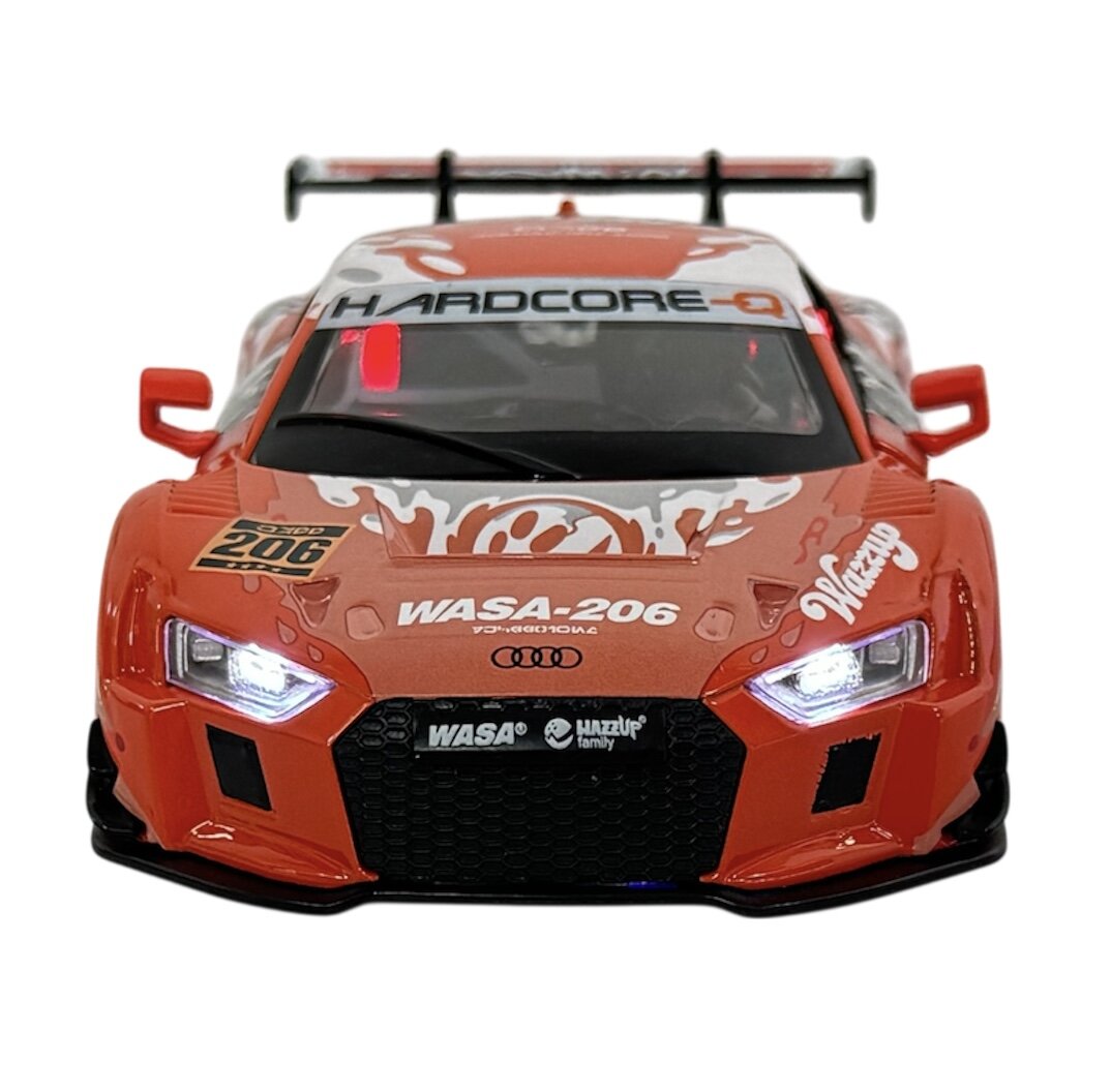 Model samochodu wyścigowego w kolorze pomarańczowym z widocznymi napisami \'HARDCORE\', \'WASA-206\', \'Wazzup\' oraz logo Audi. Samochód posiada szczegółowe elementy, takie jak reflektory i spojler.