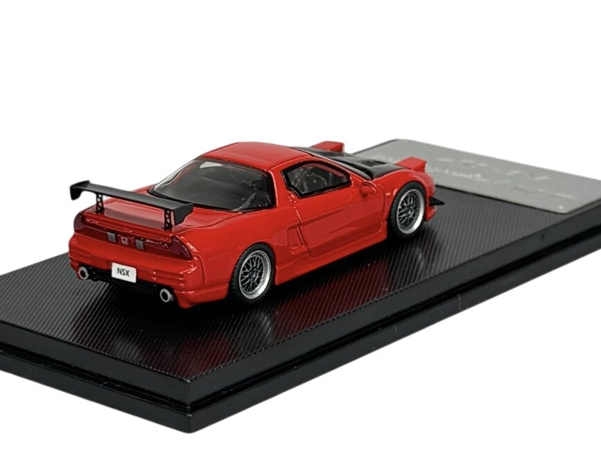Czerwony model samochodu sportowego z czarnym spojlerem, umieszczony na czarnej podstawce. Na tablicy rejestracyjnej widnieje napis \'NSX\'.
