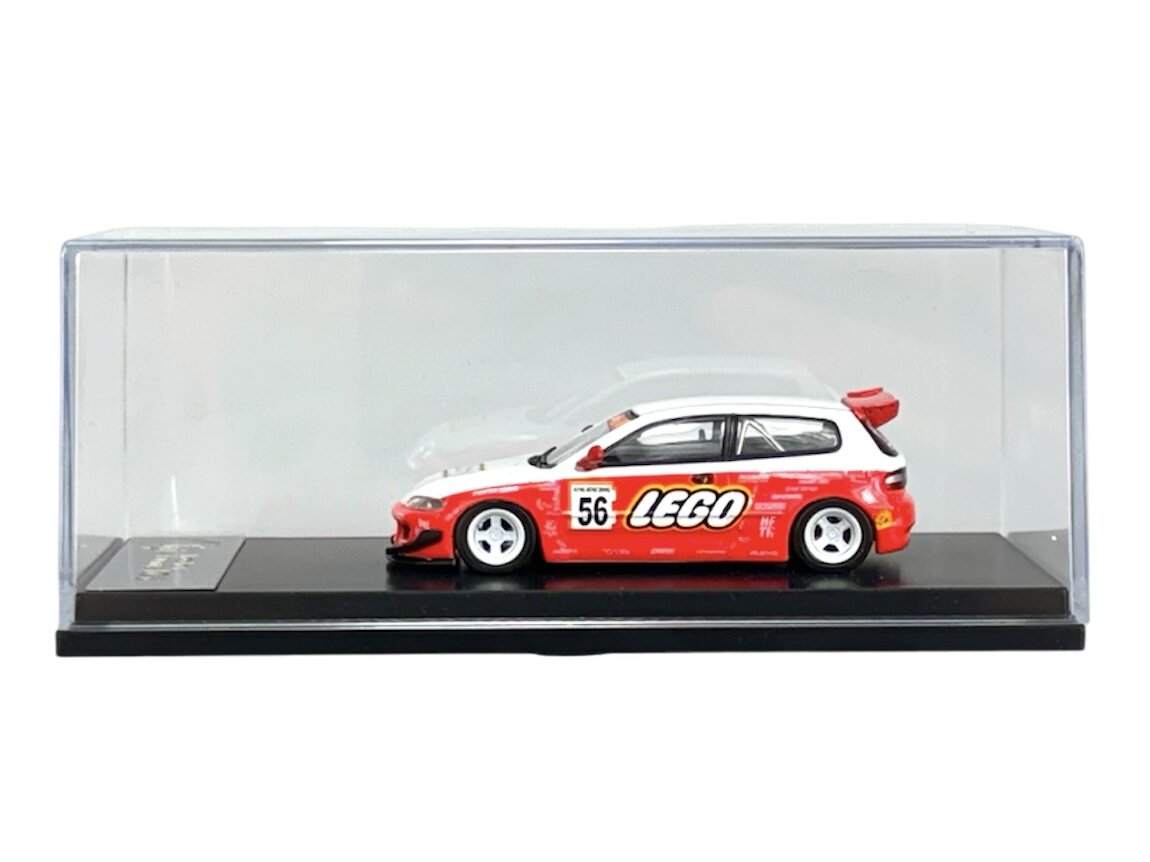 Model samochodu w skali 1:64 w kolorze czerwono-białym z dużym napisem \'LEGO\' na boku, umieszczony w przezroczystej gablocie. Na boku widoczny jest również numer \'56\'.