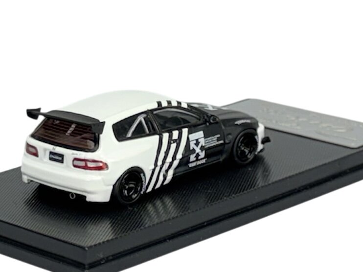 Model samochodu w skali 1:64 przedstawia czarno-białego hatchbacka z wyraźnym wzorem na boku. Auto umieszczone jest na czarnej podstawce z teksturą.